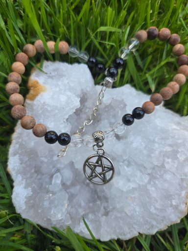 Bracelet de cheville Bracelet en perles en bois et métal avec un pendentif pentacle, posé sur un cristal.